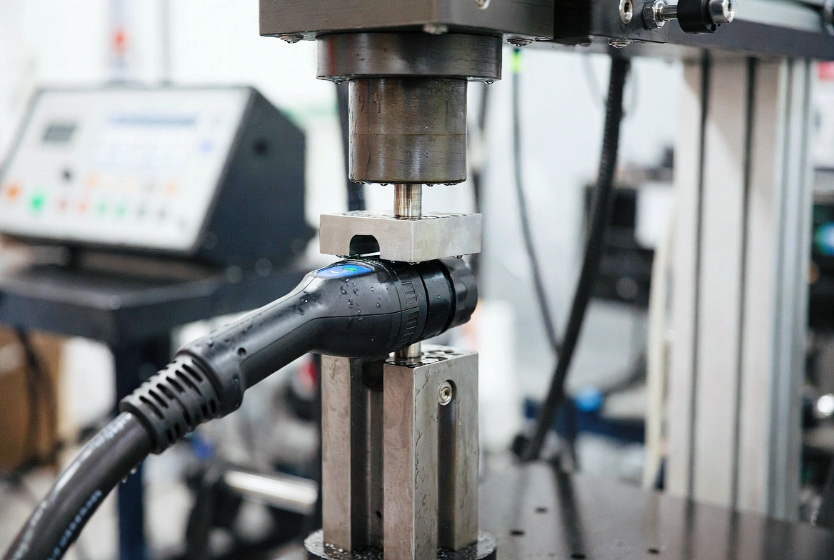 How to Test an EV Charger: Complete Guide to IEC 61851-23 & UL 2251 Compliance 3 Charging gun securely clamped in the pull torque tester fixture, mechanical arm applying controlled force, realistic water droplets or mechanical detail visible, sharp technical product photography, professional lab setting.