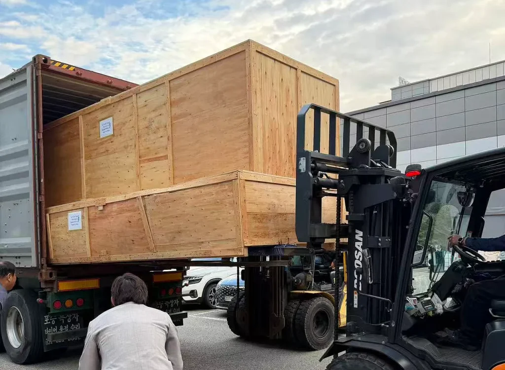 Oversized wooden crates for the KINGPO KP-DC4000 walk-in sand and dust test chamber being handled by forklift beside a shipping container in South Korea.