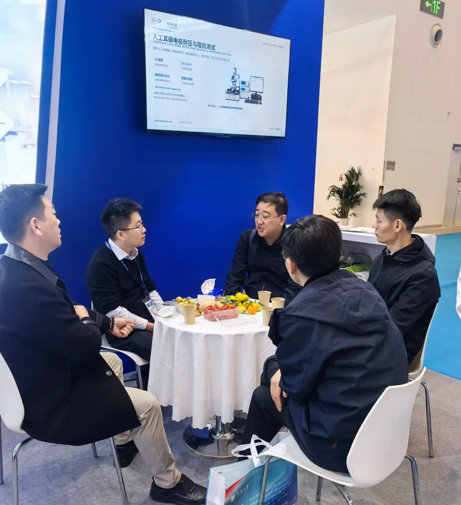 KINGPO Presents an Integrated Testing Solution for Implantable Brain-Computer Interfaces at CMEF 2026 5 Visitors discussing implantable medical device testing at KINGPO's CMEF booth with a display showing cochlear electrode withstand voltage testing