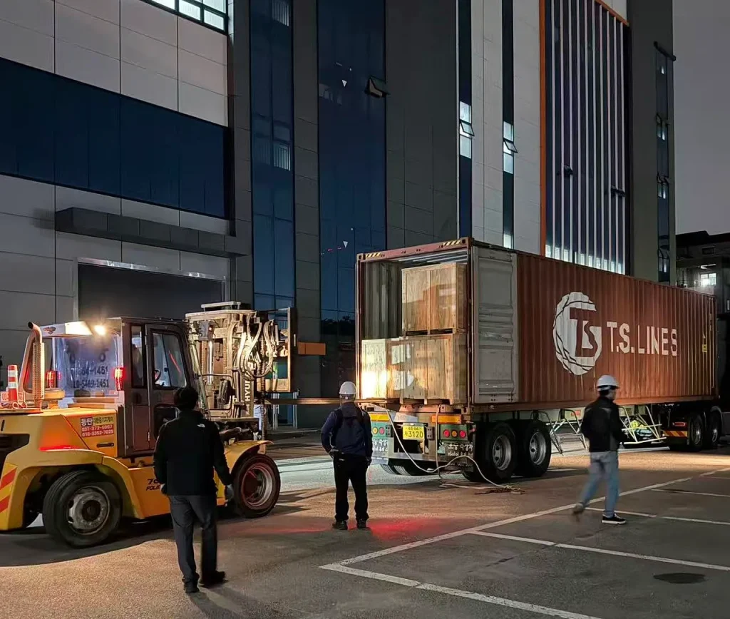 Shipping container and forklift at the Korean installation facility during nighttime unloading of KINGPO KP-DC4000 walk-in dust chamber components.