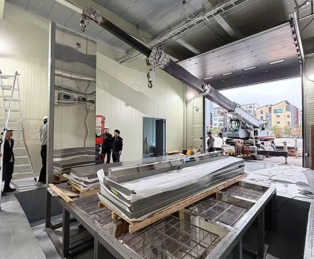 Mobile crane positioned outside the laboratory with large metal chamber sections inside during installation of KINGPO's 64 m³ walk-in dust test chamber in Korea.